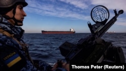 Un militar al gărzii de coastă a Ucrainei în timpul unei patrule, în timp ce o navă de marfă în larg în Marea Neagră, februarie 2024.