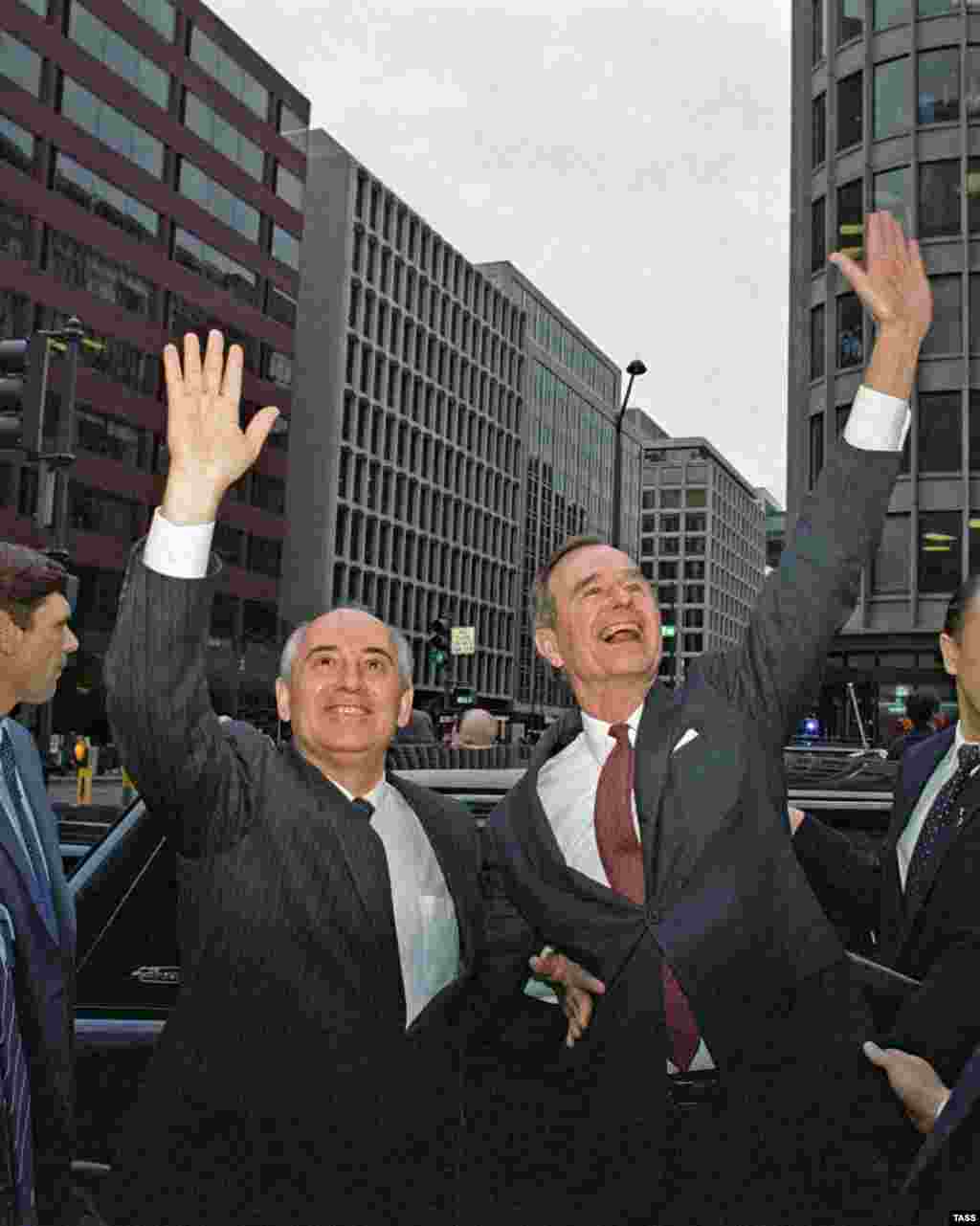 Secretarul general al Comitetului Central al PCUS, Mihail Gorbaciov, și vicepreședintele Statelor Unite ale Americii, George Bush (de la stânga la dreapta), salută locuitorii orașului Washington&nbsp;pe o stradă.&nbsp;