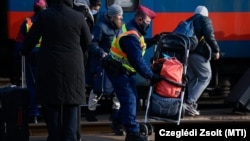Egy, az orosz–ukrán háború elől menekülő nő babakocsiját rakja a peronra egy rendőr a záhonyi vasútállomáson 2022. március 1-jén