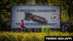Budapesta, 18 octombrie, un bărbat trece prin fața unui banner care înfățișează o bombă, cu textul: „Suntem pedepsiți de sancțiunile Bruxelles-ului!”.
