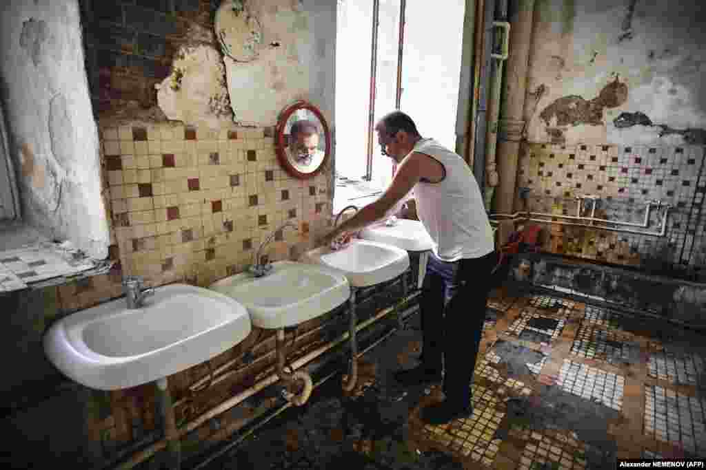 Vladimir Mogilnikov, 62 de ani, își spală mâinile în baia comună. &bdquo;Aici stau claie peste grămadă sute de oameni, adesea câte cinci într-o cameră cu pereți mucegăiți și țevi ruginite, care scurg&rdquo;, spune el.