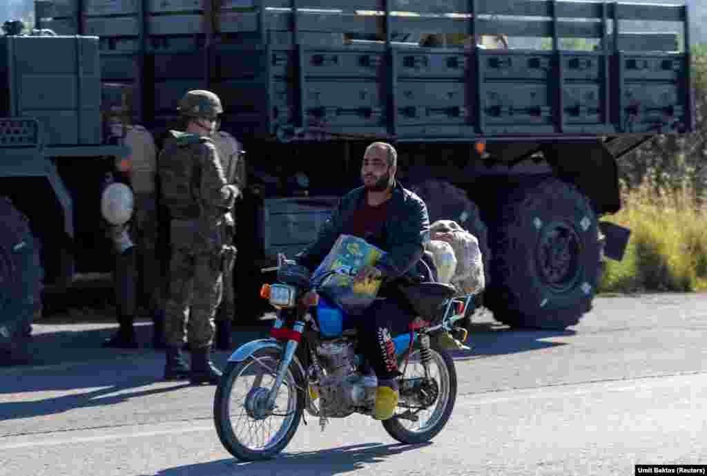 Un localnic, trecând pe lângă un convoi rusesc, în apropiere de baza aerienă Hmeimim. „Localnicii doar urmăresc ce se întâmplă”, spune fotograful turc despre situația din jurul bazei, care nu mai dispune de protecția militară externă oferită până recent de armata lui Assad. „În satul din apropierea bazei aeriene, există o mulțime de magazine cu inscripții în rusă, dar toate sunt acum închise. Nu vezi soldați ruși care să iasă din bază singuri sau în mașini neblindate”, mai spune Umit Bektas.