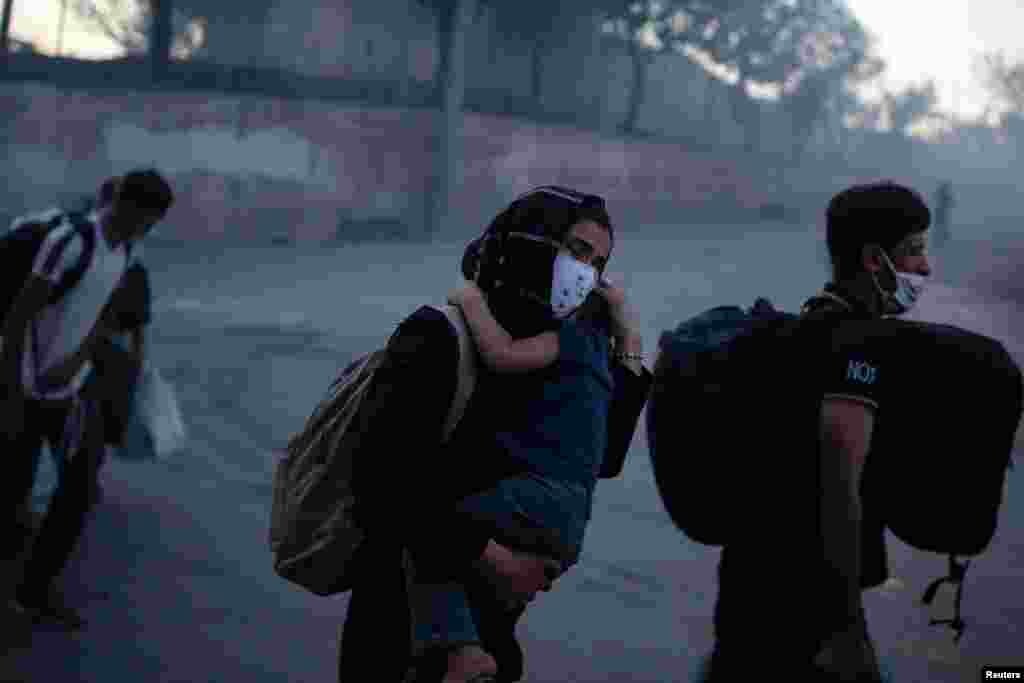 Disa migrantë shihen duke u larguar nga ambientet e kampit teksa mbajnë në duar fëmijë të vegjël.
