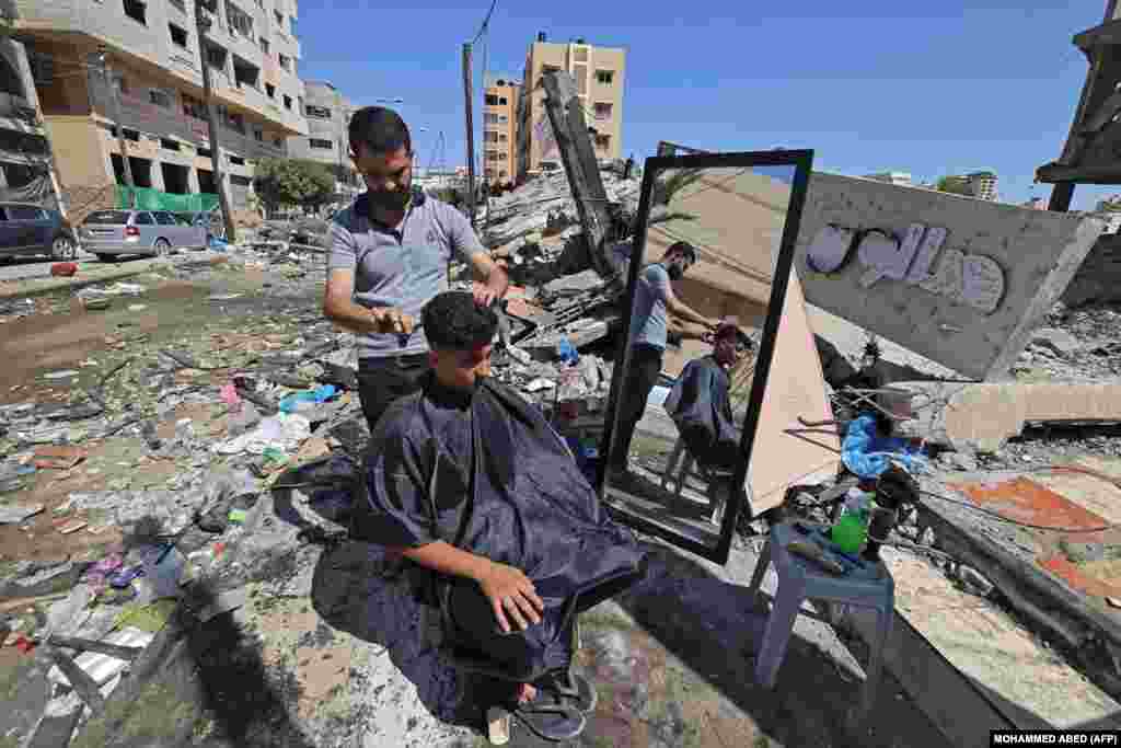 Një berber palestinez qeth një person pranë rrënojave të ndërtesave të shkatërruara në qytetin e Gazës. 25 maj, 2021. &nbsp;