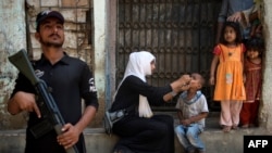 FILE: A Pakistani policeman stands guard as a health worker administers the polio vaccine to a child during a vaccination campaign in Karachi, April 2017.