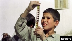Un băiat afgan examinează o bandă de film smulsă din flăcările unui foc de tabără aprins de talibani pentru a distruge rolele de cinema în Kabul în 1996. 