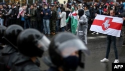 A man carrying the former white-red-white flag of Belarus stands in front of riot police during a rally to protest against the presidential election results in Minsk on October 11, 2020.